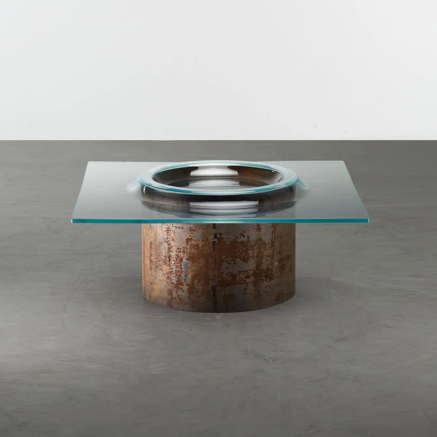 A modern art sculpture with a glass bowl-like structure on a rusty cylindrical base.