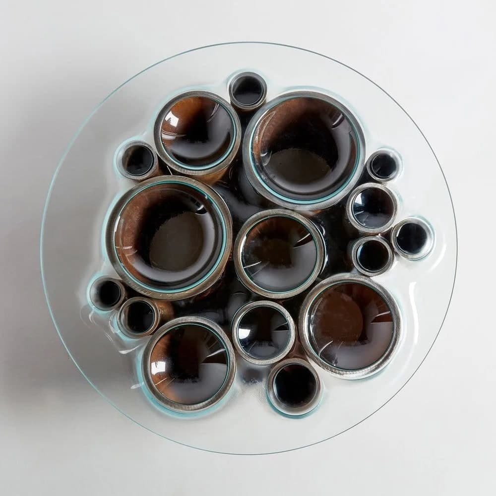 Top-down view of various glass bottles with dark liquid, arranged in a circular pattern on a transparent plate.