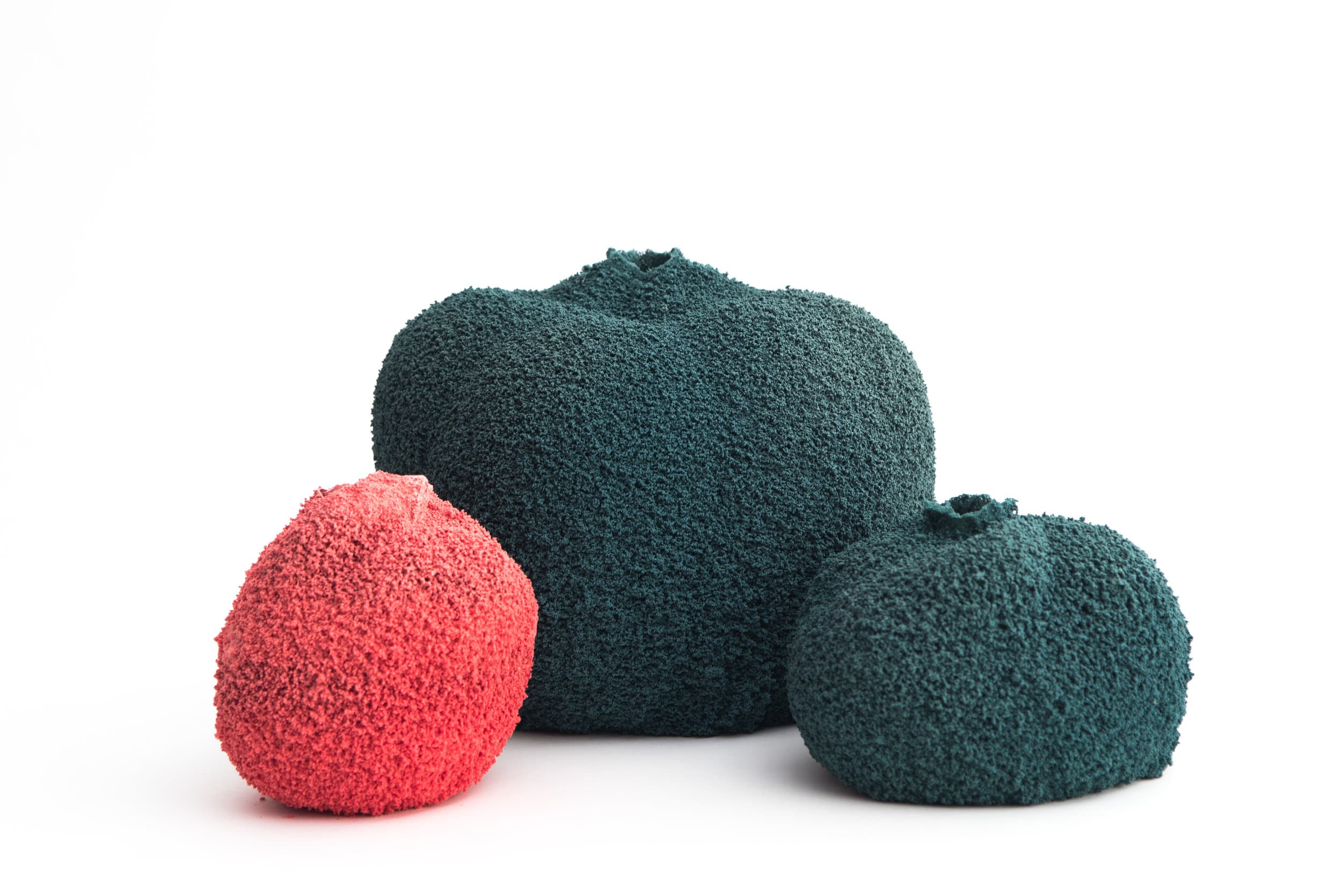 A coral-red vessel beside two teal Else Coral porcelain forms by Michal Fargo