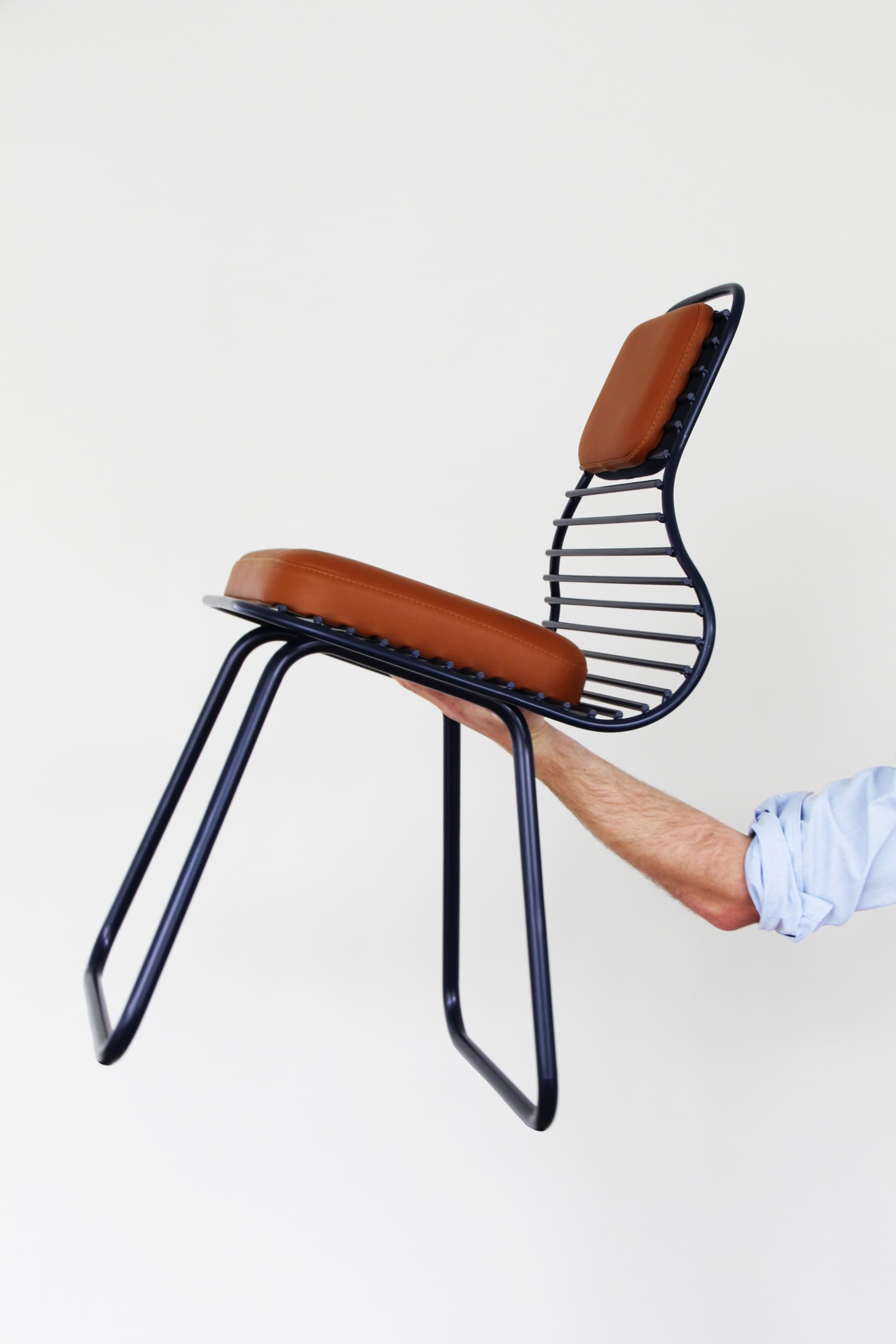 Chair 01 by Daphna Laurens for Wittmann, held in profile to reveal the open steel frame and brown leather cushions