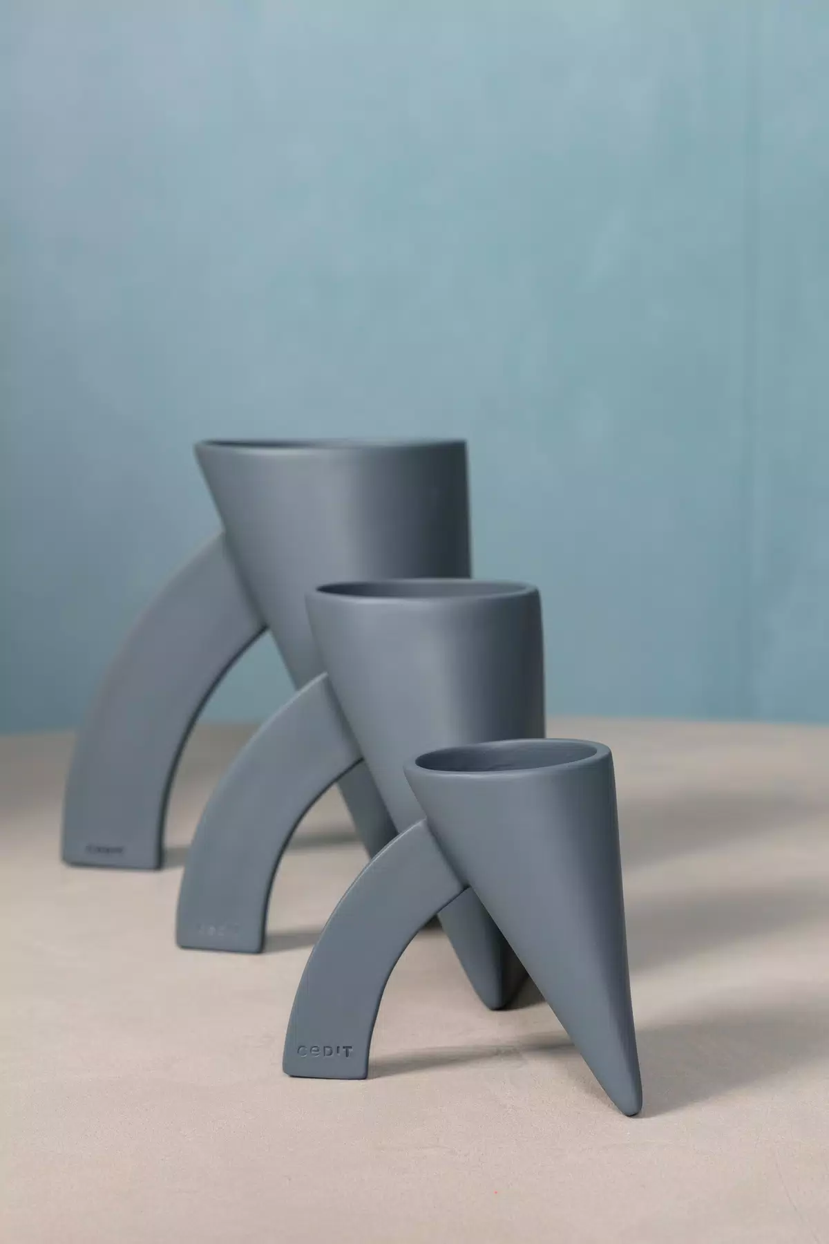 Three grey Lapis re-edition vases in the collection’s three sizes, photographed against a pale blue background