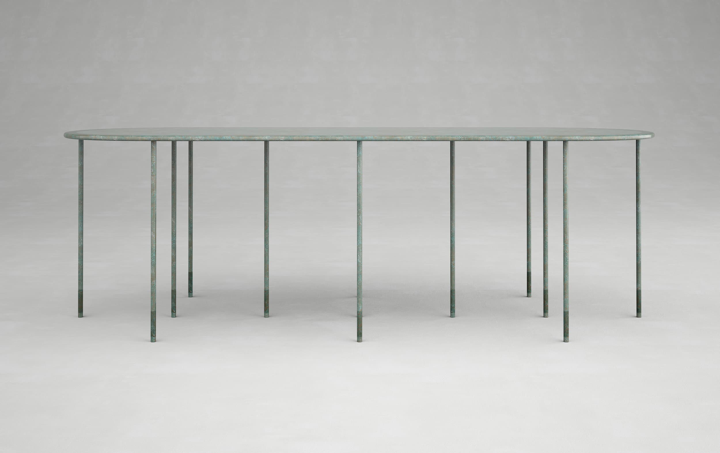 Long blue-green table with a thin rounded top and many slender legs against a grey background.