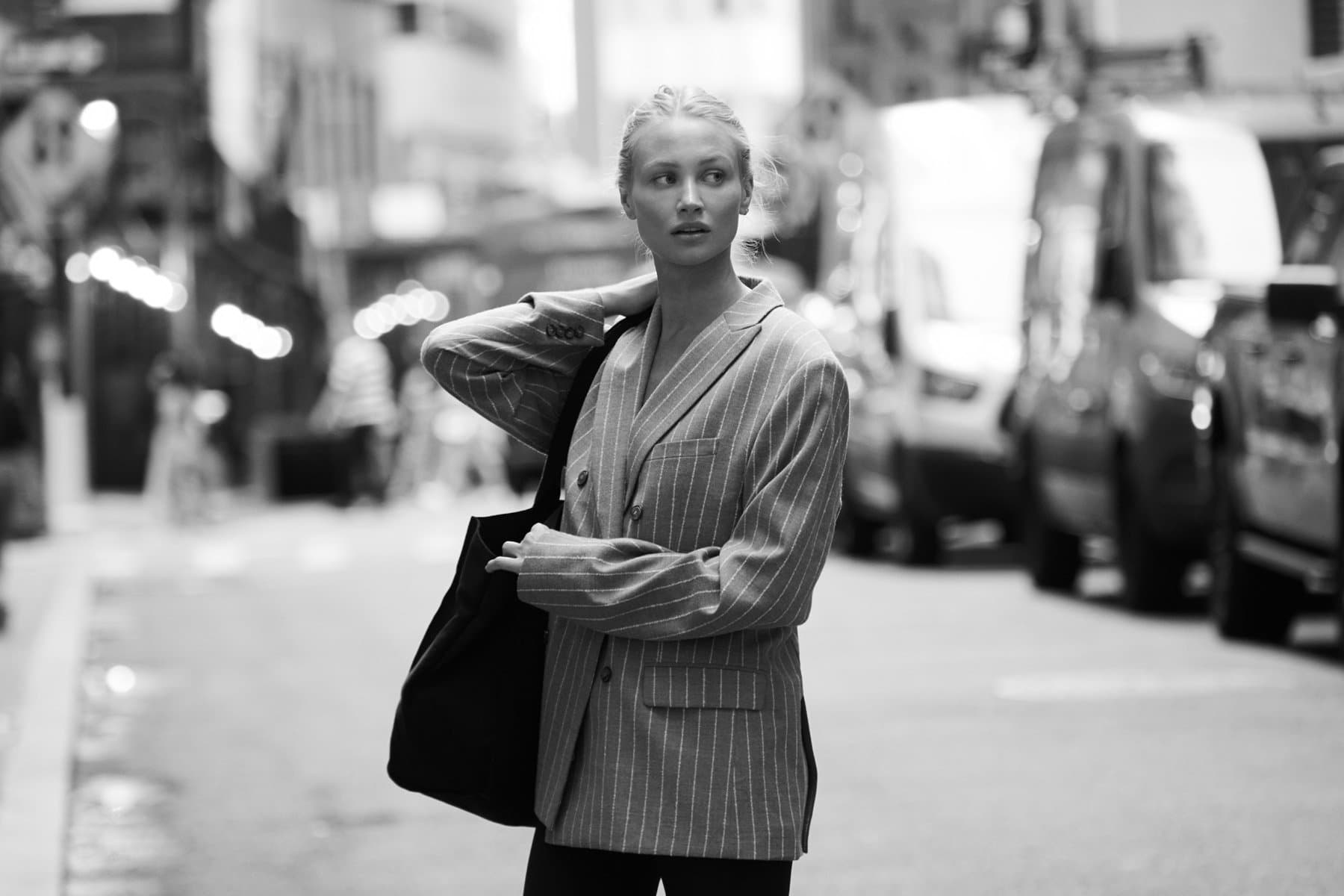 A black-and-white fashion portrait of a woman in a striped blazer on a New York street.