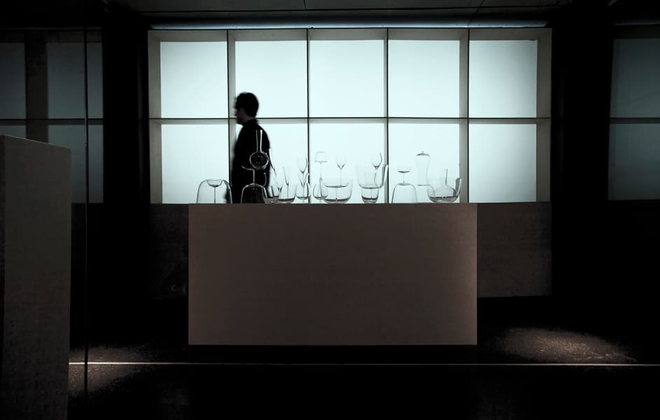 Misfits glass assemblages on an exhibition plinth, with a passing silhouette behind them.