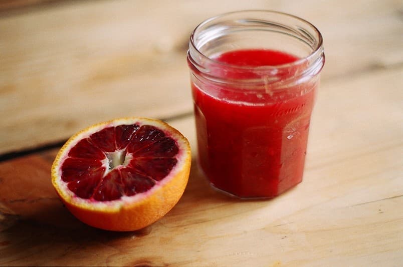 A blood orange and a jar of juice on a sunlit wooden table.