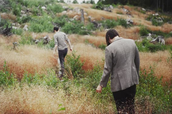 Two people walking away through grasses and low vegetation.