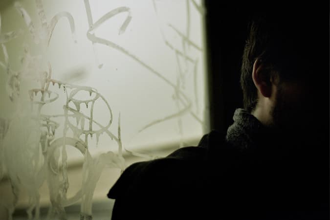 A partly shadowed figure beside a pane of marked glass.