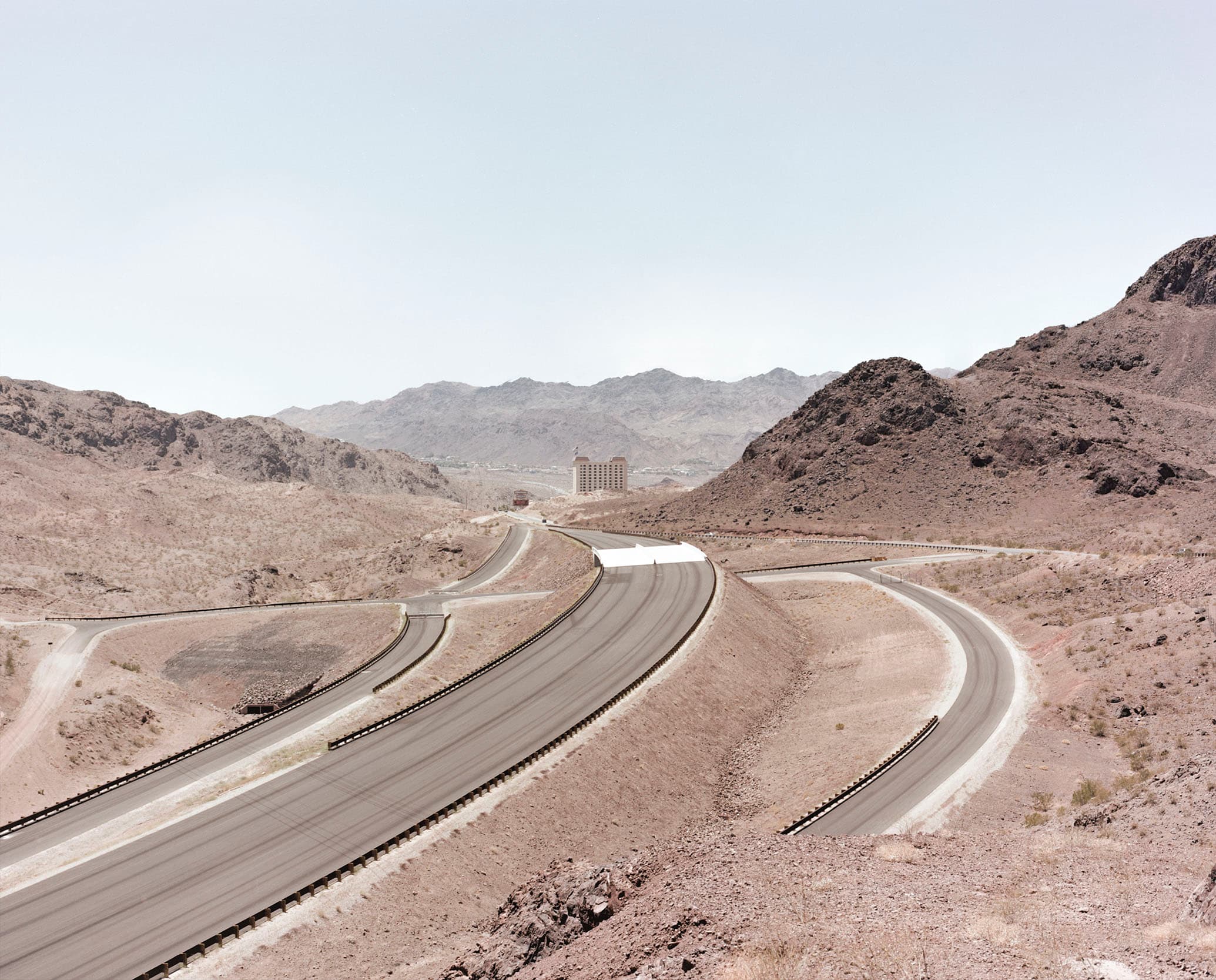 Empty roads winding through an arid mountain landscape toward a distant hotel.