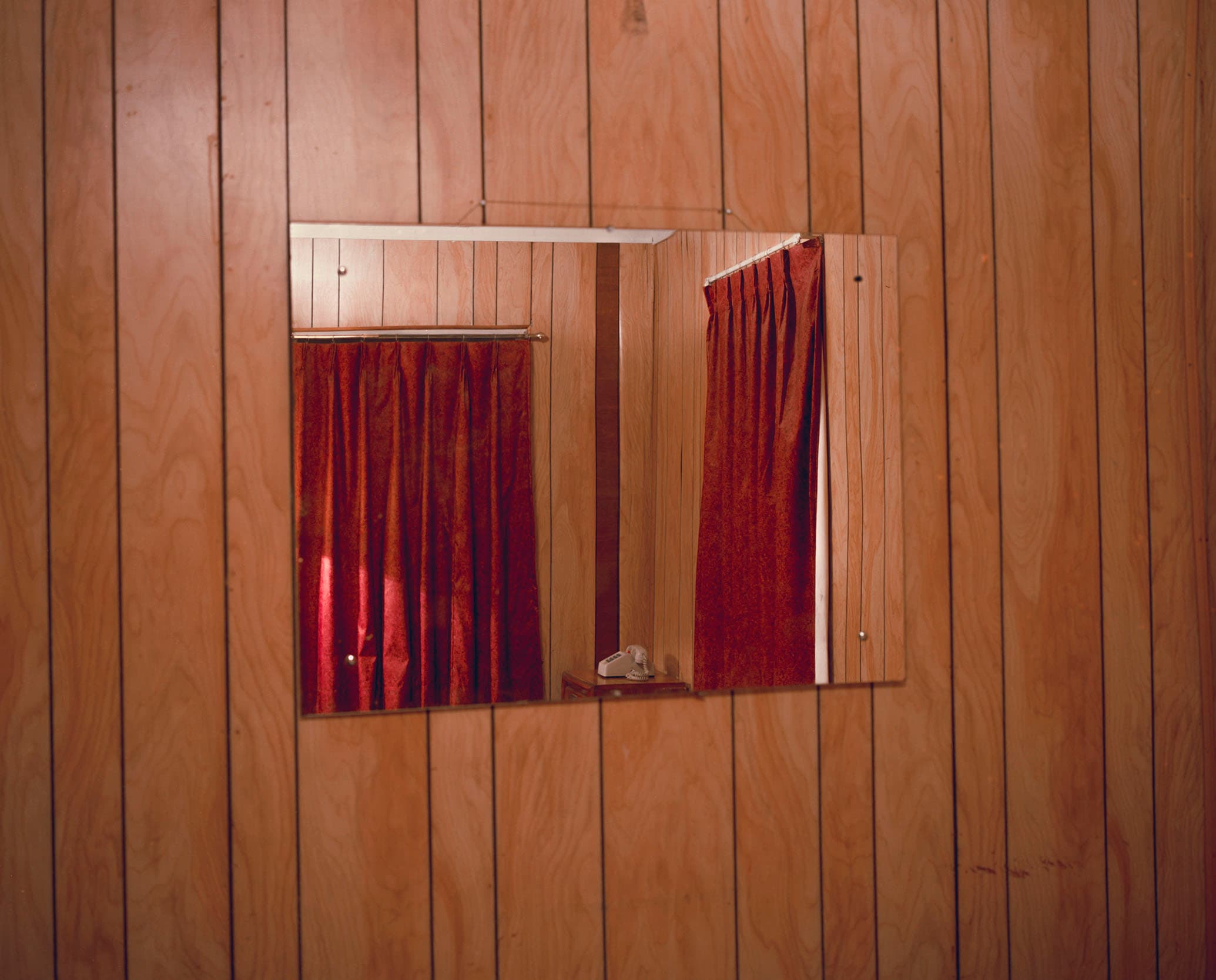 A wall mirror reflecting red curtains and a telephone in a wood-panelled room.