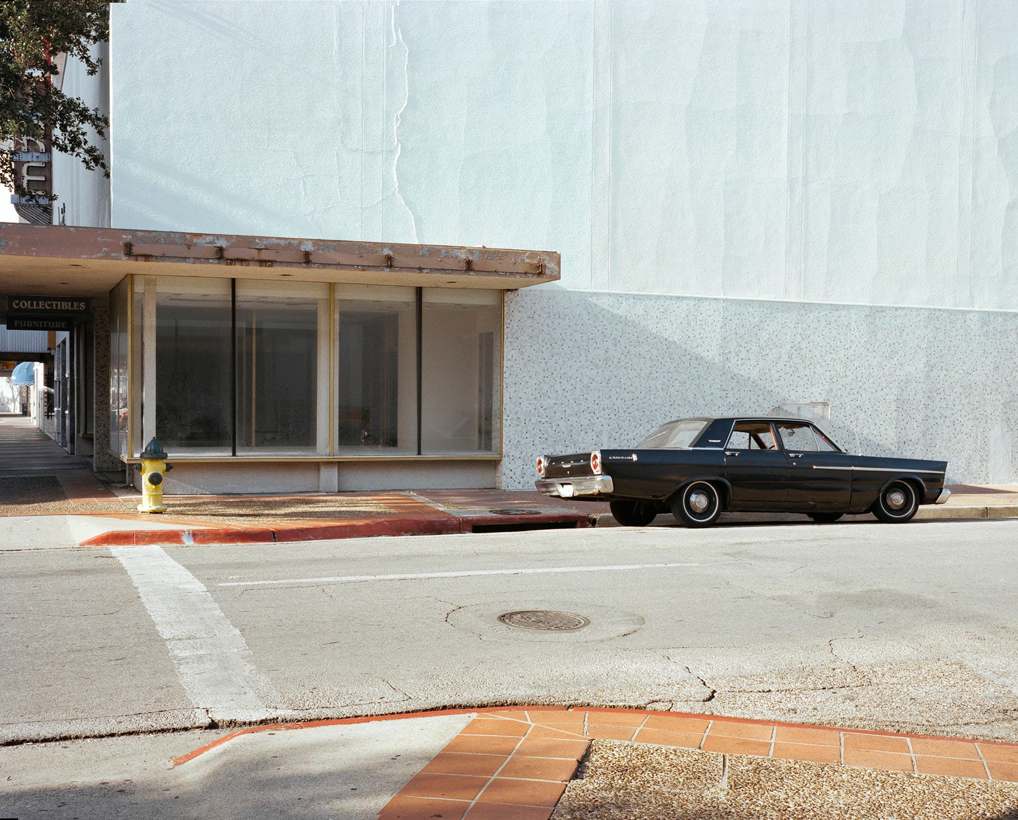 A dark vintage sedan parked beside a pale turquoise building.