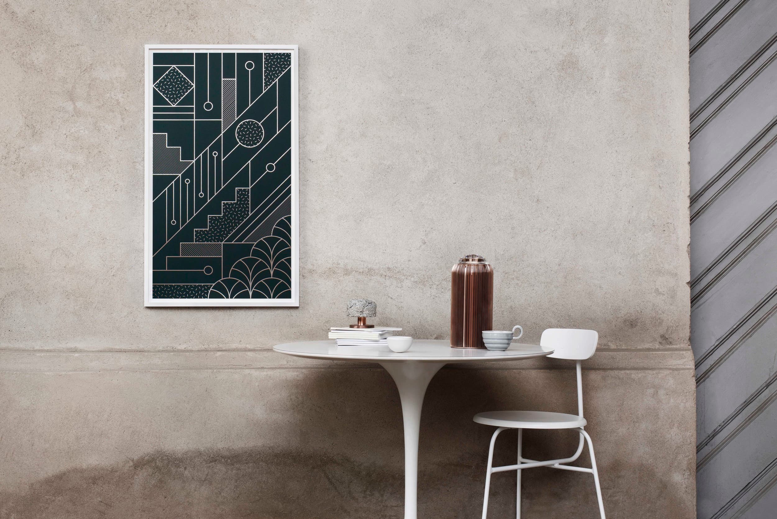 A framed dark-green graphic print by Kristina Krogh, with pale geometric lines and curved patterns, displayed above a table.