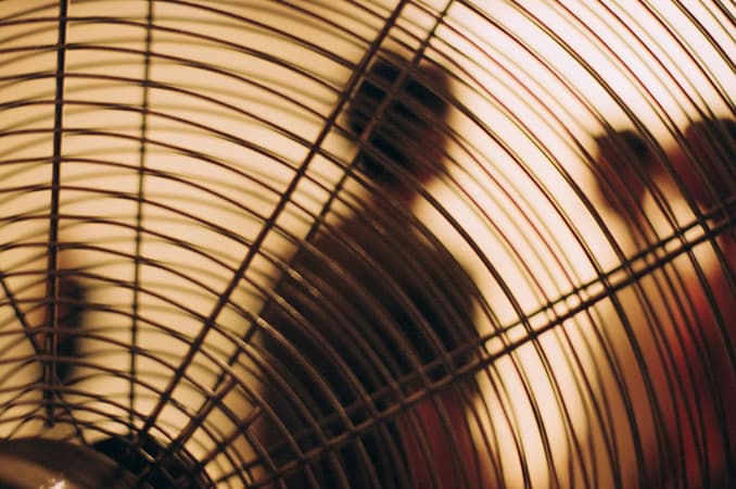 A figure behind the intersecting lines of a fan grille.
