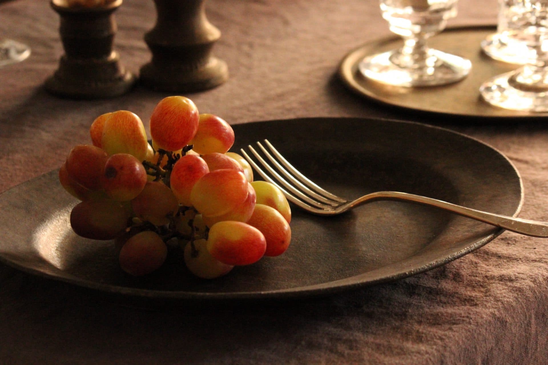 Dark rustic oval ceramic plate by Yumiko Yasufuku, holding grapes and a fork.