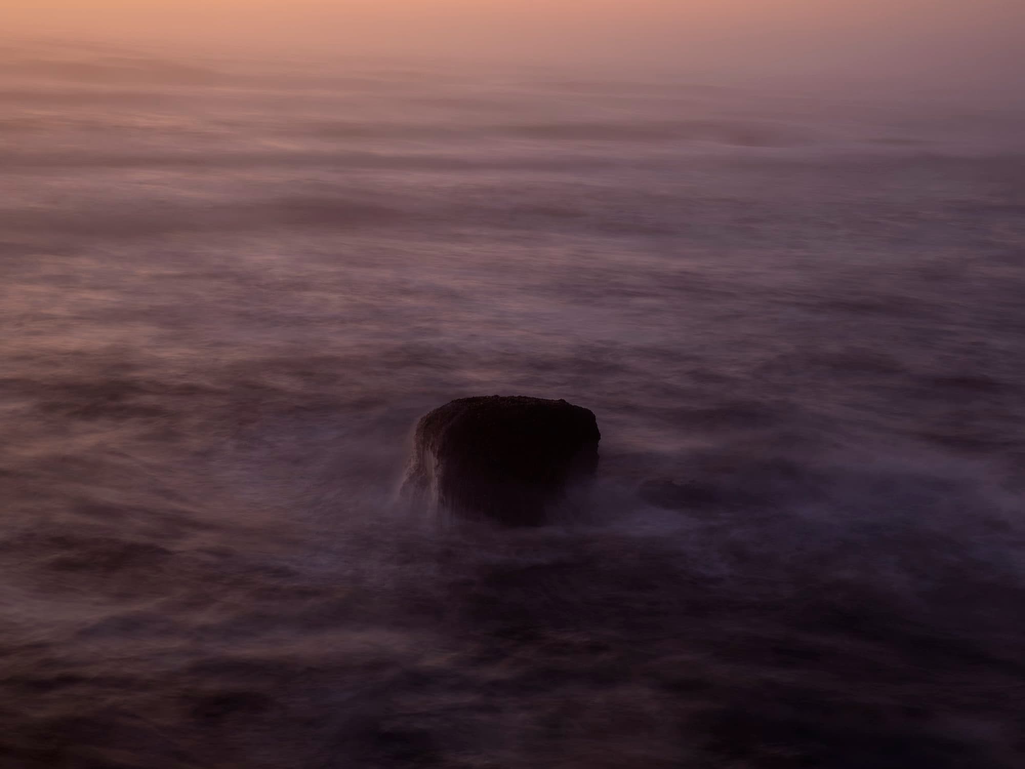 Rock and sea in soft pink-purple light.