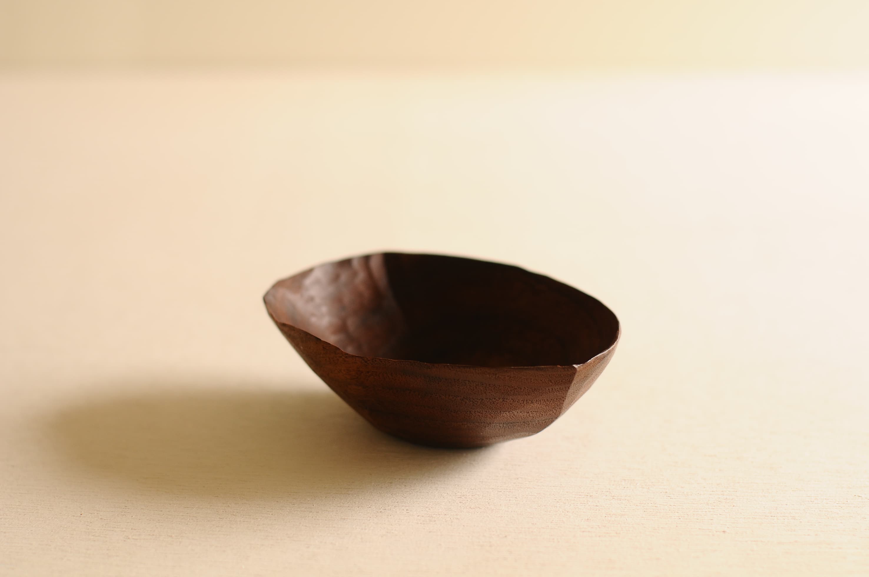 An irregular hand-carved wooden bowl by Toru Sugimura, shown against a neutral background.