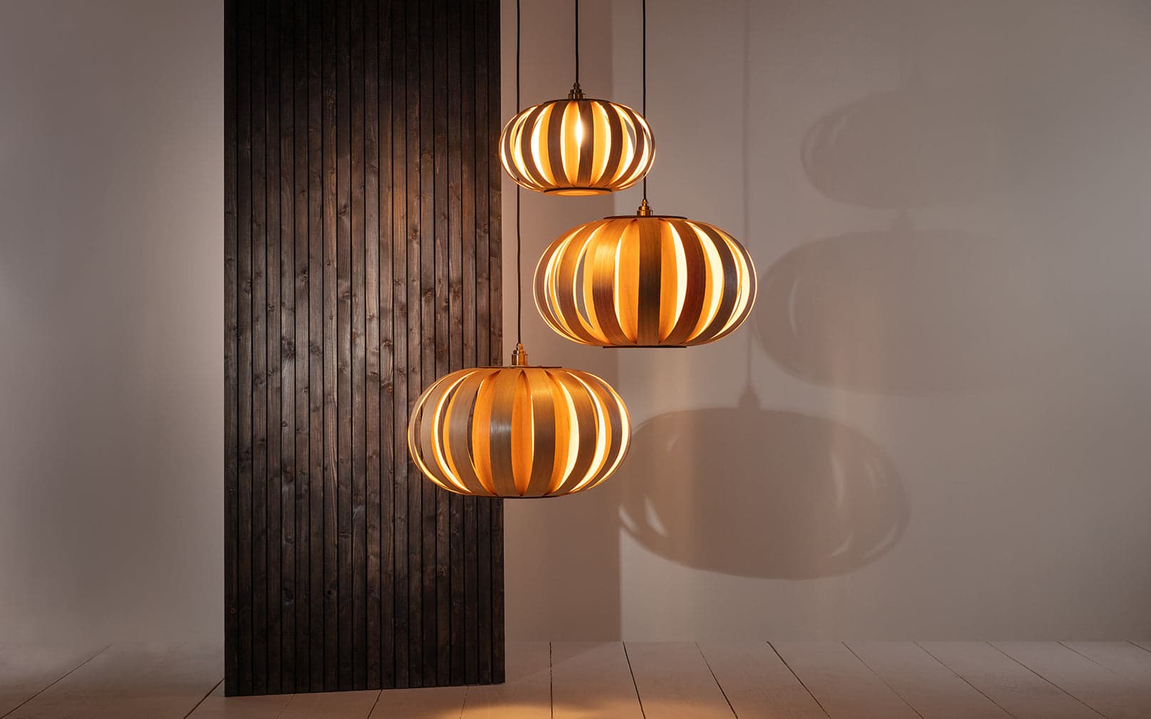 Urchin Pendant Range Cluster by Tom Raffield in oak, shown as three illuminated wooden pendants.