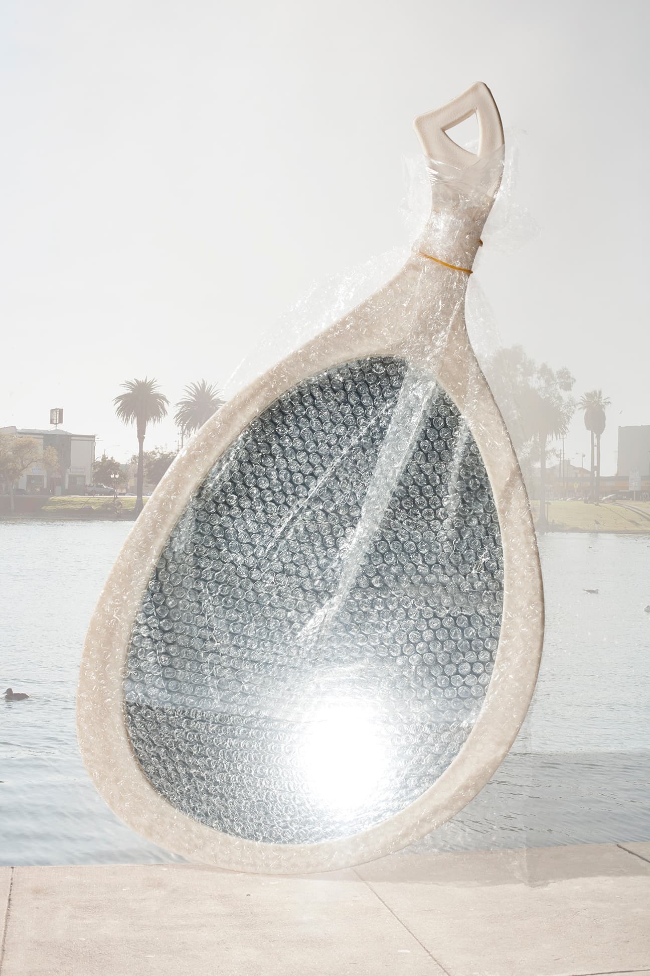 A hand mirror wrapped in bubble wrap is superimposed over a bright waterside scene with palm trees.