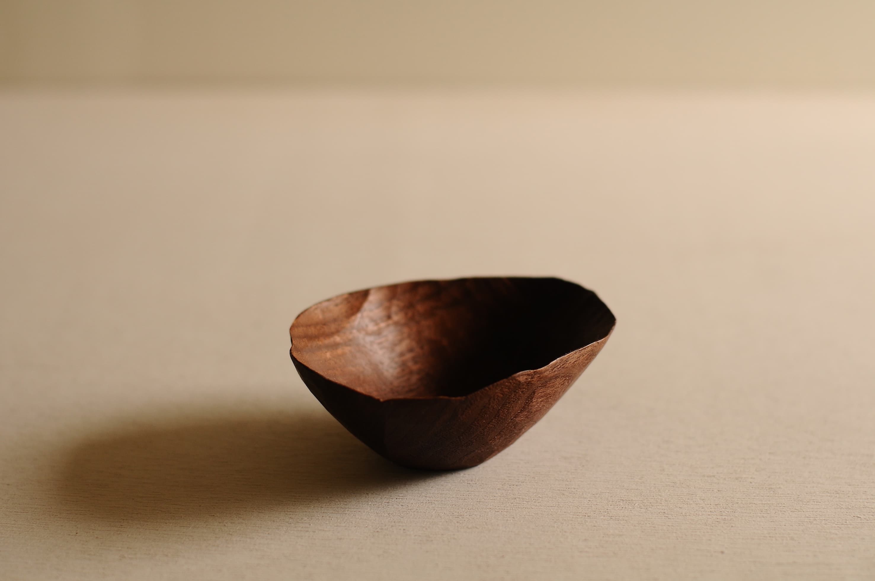 An irregular hand-carved wooden bowl by Toru Sugimura, shown against a neutral background.