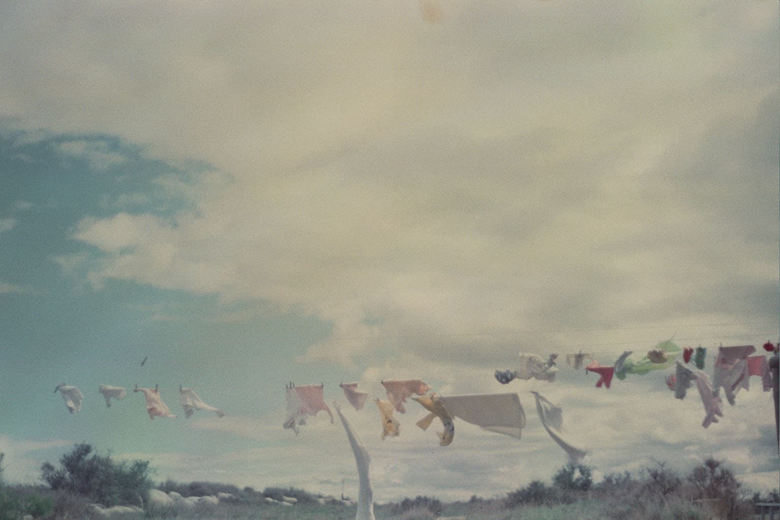 Windblown laundry hangs over rocky ground beneath a broad, cloud-filled sky.