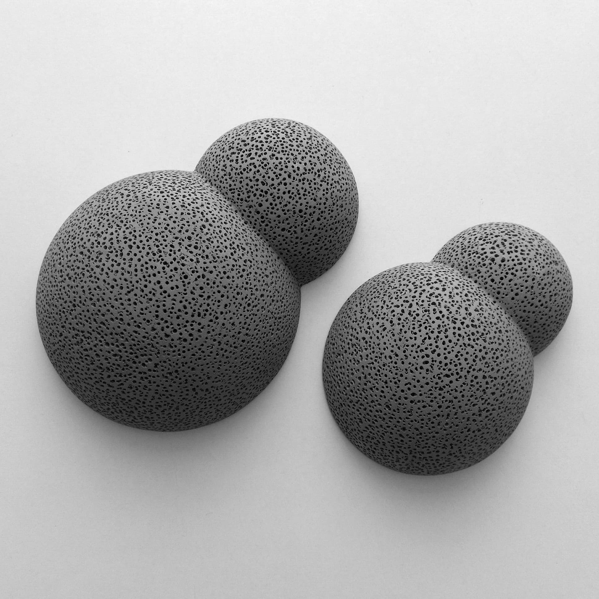 Four rounded dark sculptural objects with densely textured surfaces