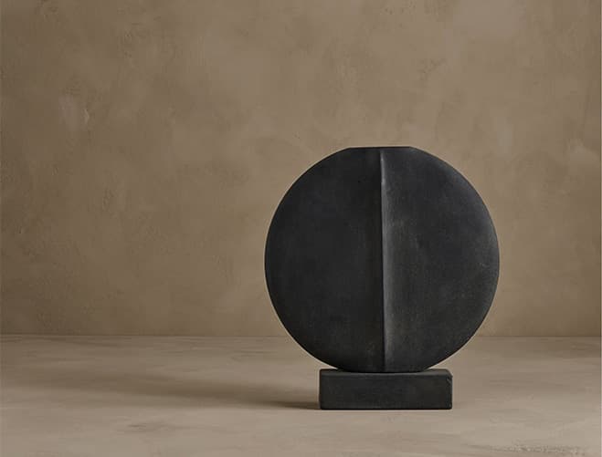 A dark round ceramic sculptural form on a small rectangular base
