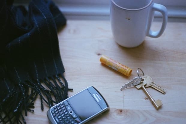 A BlackBerry phone, keys, lip balm, mug and scarf lie on a wooden tabletop.