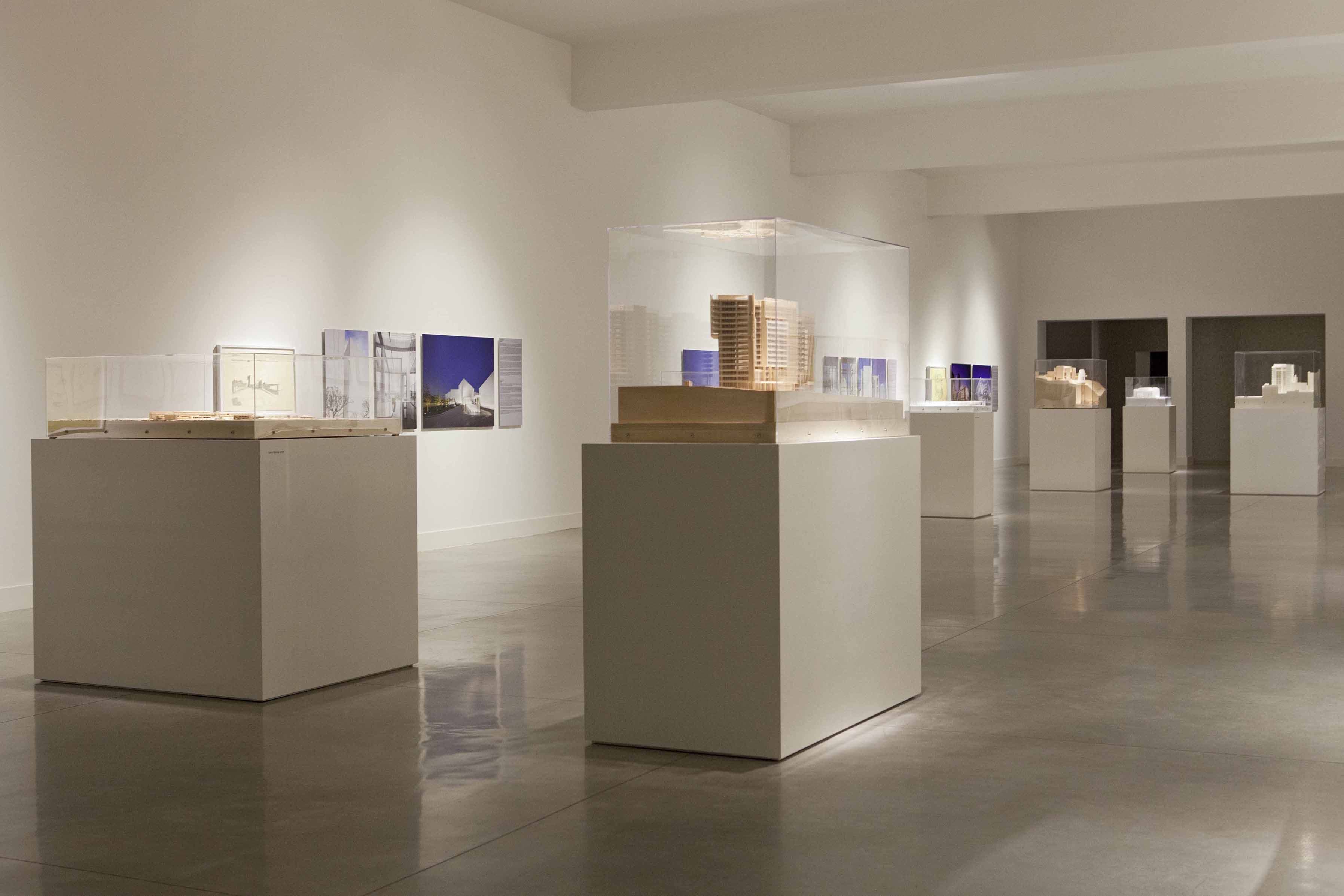 Architectural models in transparent cases on white plinths, with drawings and photographs on the gallery walls.