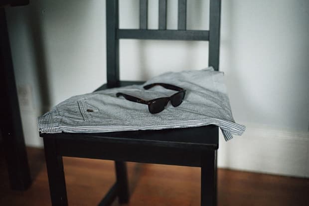 Sunglasses rest on a striped shirt draped over a dark wooden chair.