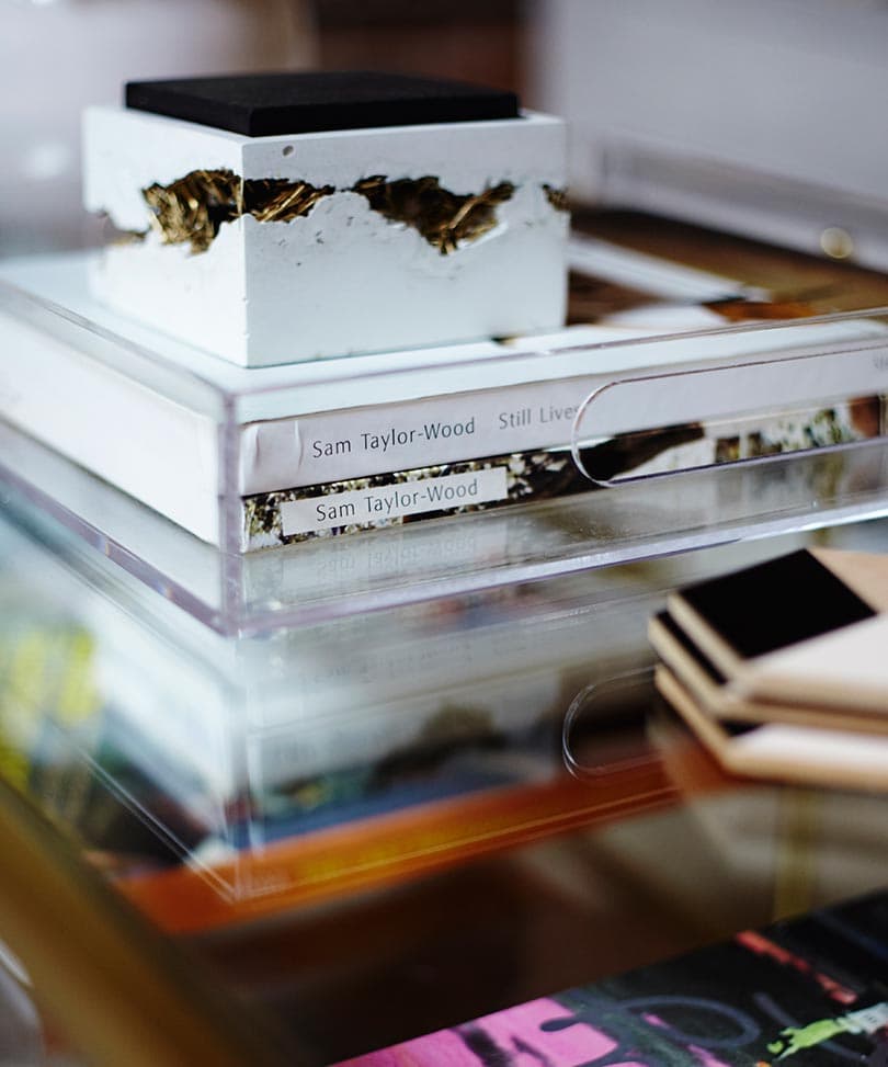 A white concrete box with gold-colored inclusions and a dark square lid sits on books in a clear acrylic tray.