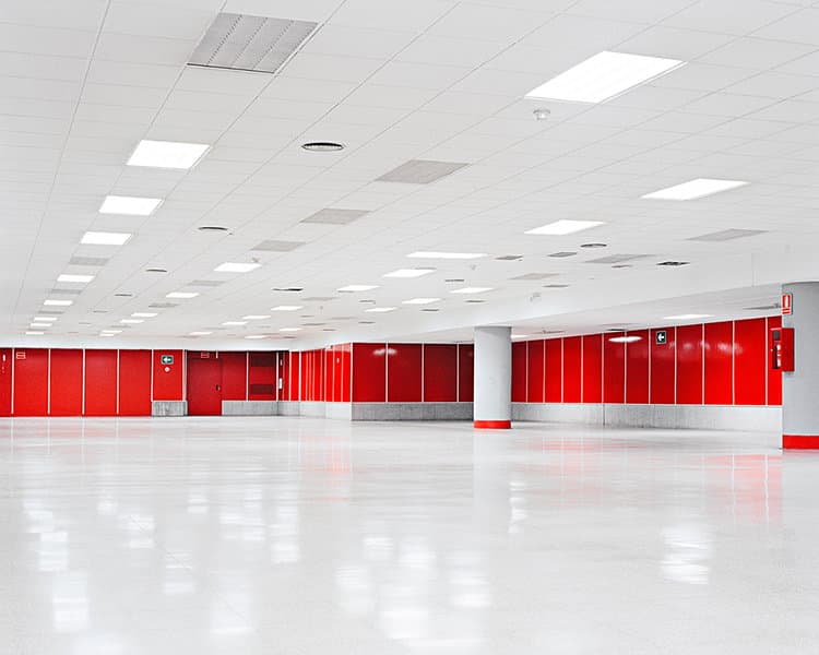 An empty hall has bright red wall panels, white ceiling tiles and a reflective pale floor.