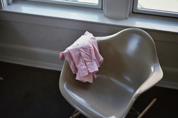 A pink shirt hangs over a pale molded chair beside a window.