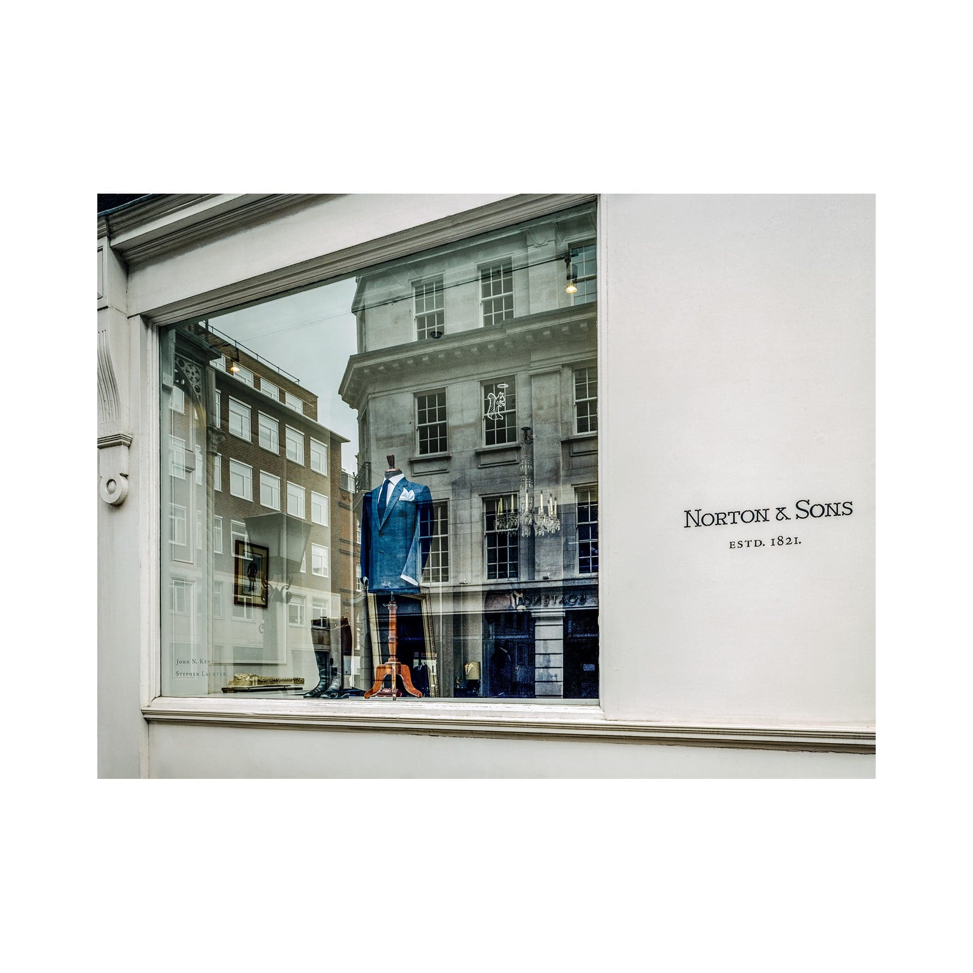 Norton & Sons tailor shop window on Savile Row, with a blue suit on a dress form and reflections of the opposite London buildings.
