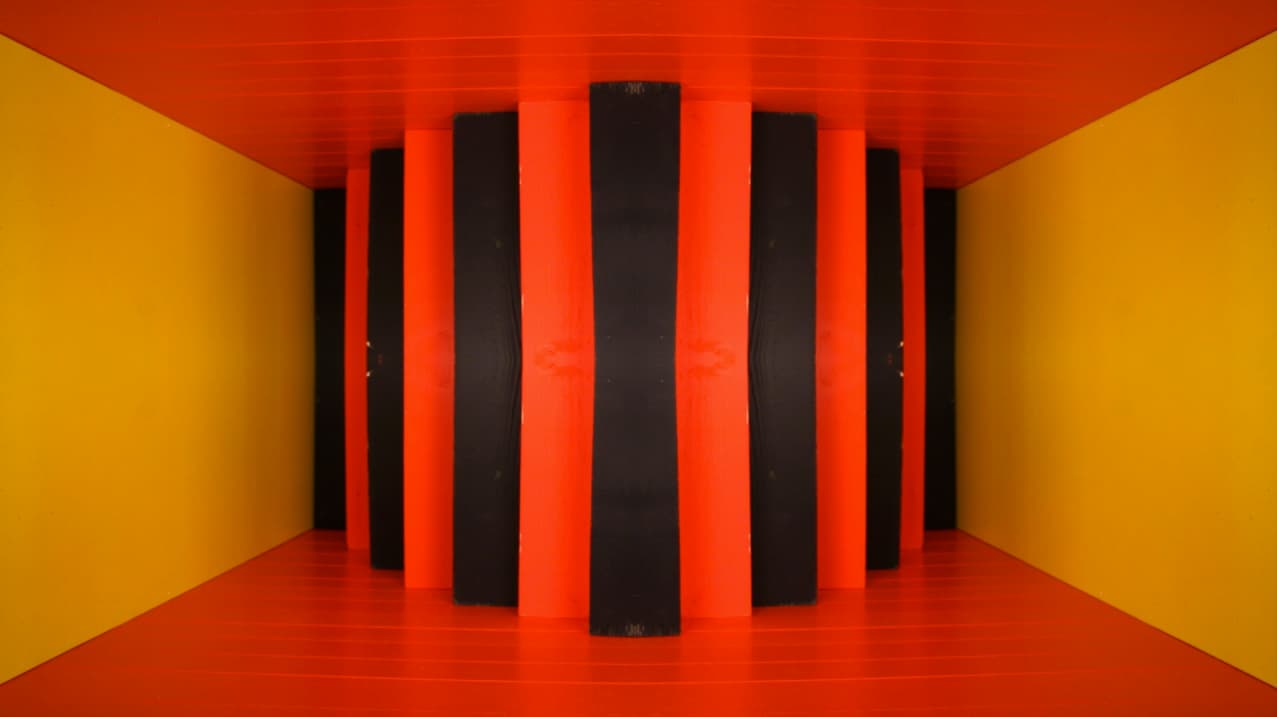 Alternating black and orange-red upright wooden blocks fill a yellow-sided box with an orange-red floor and ceiling.