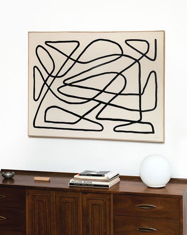 A line-based painting by Benjamin Ewing, shown above a wooden sideboard.