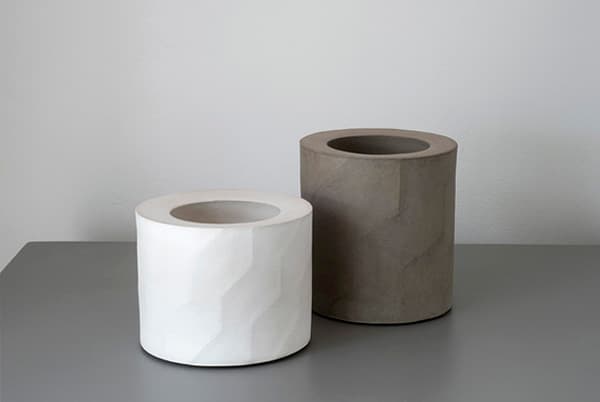 Two pale and dark cylindrical vessels by Ann Jansson with smooth rims and faceted surfaces.