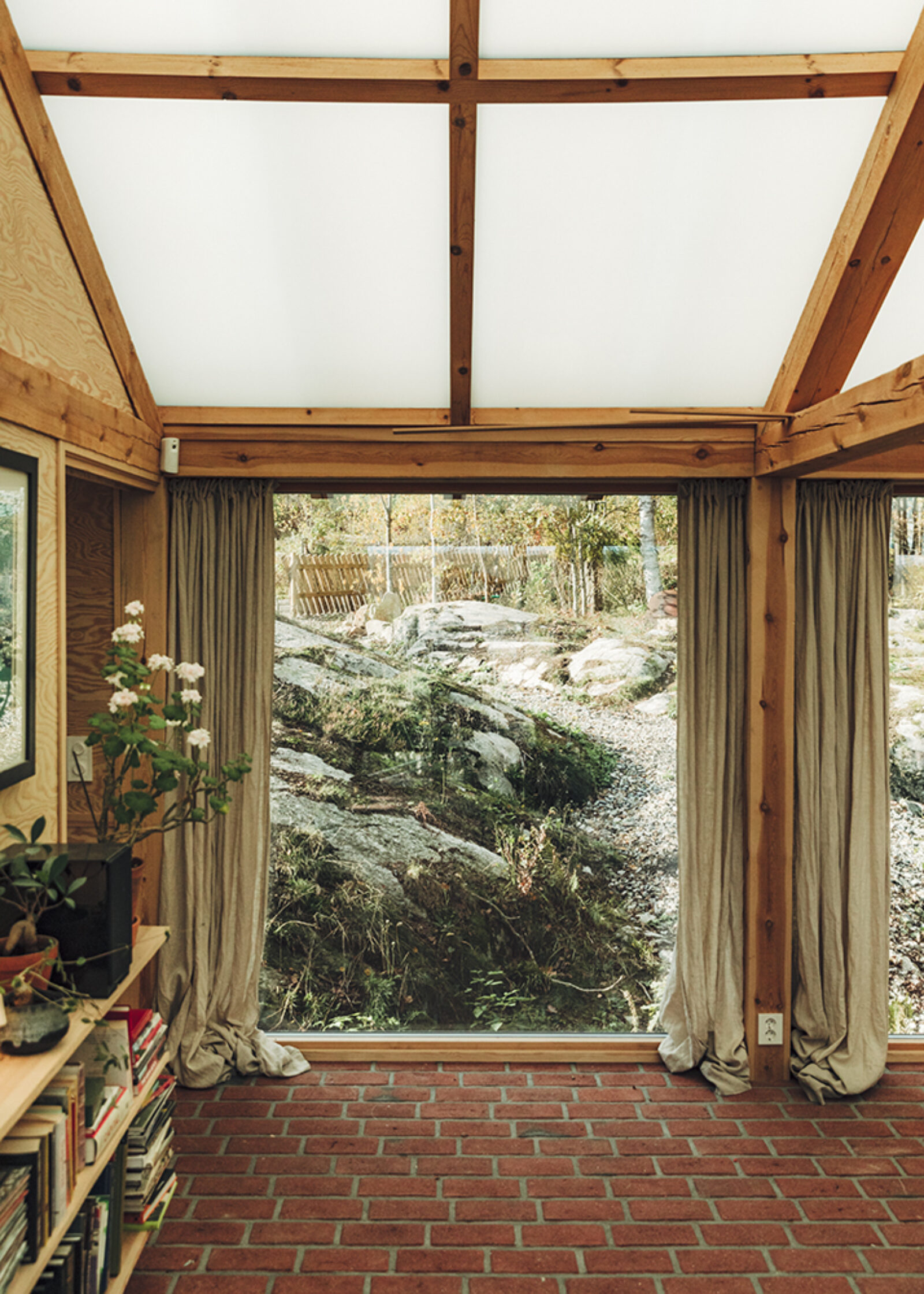 A timber-framed room with brick floor facing a large rock outside.