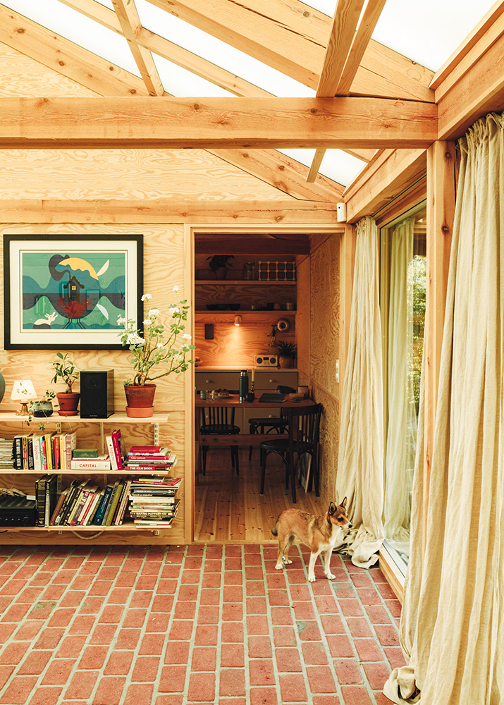 An interior view through exposed timber framing, bookshelves and the brick floor.